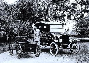 Vintage photo of man next to two cars.